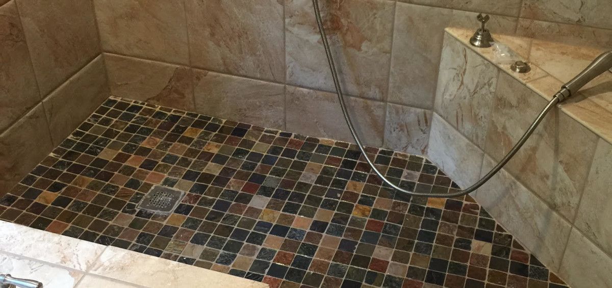 Tiled shower with multi-colored stone floor and shower head.