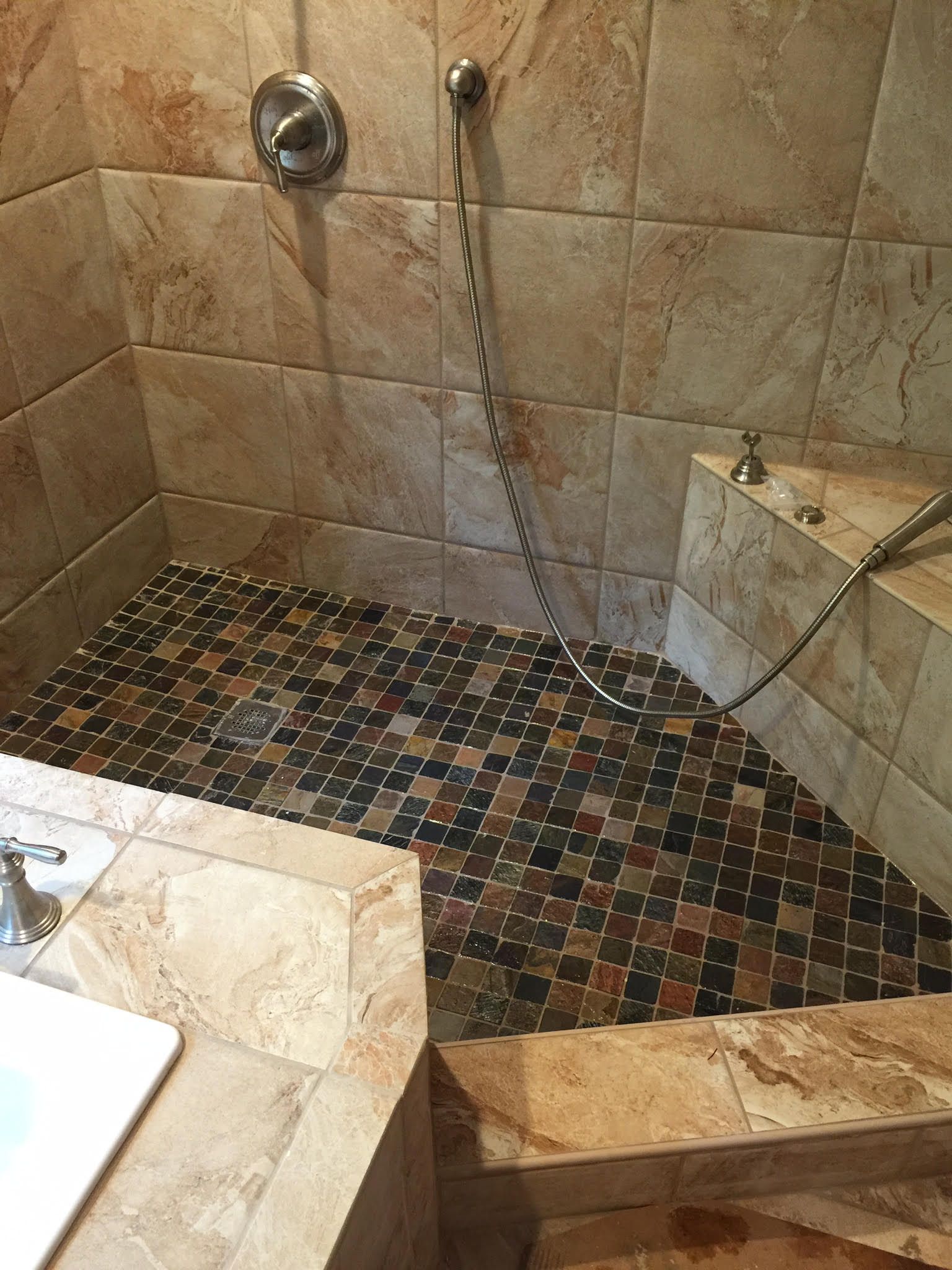 Shower with brown and black mosaic tile floor and beige walls.
