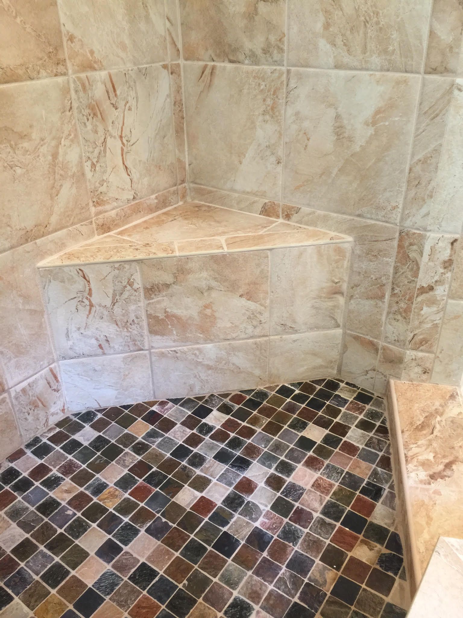 Shower stall with a built-in corner seat and mosaic tile floor.
