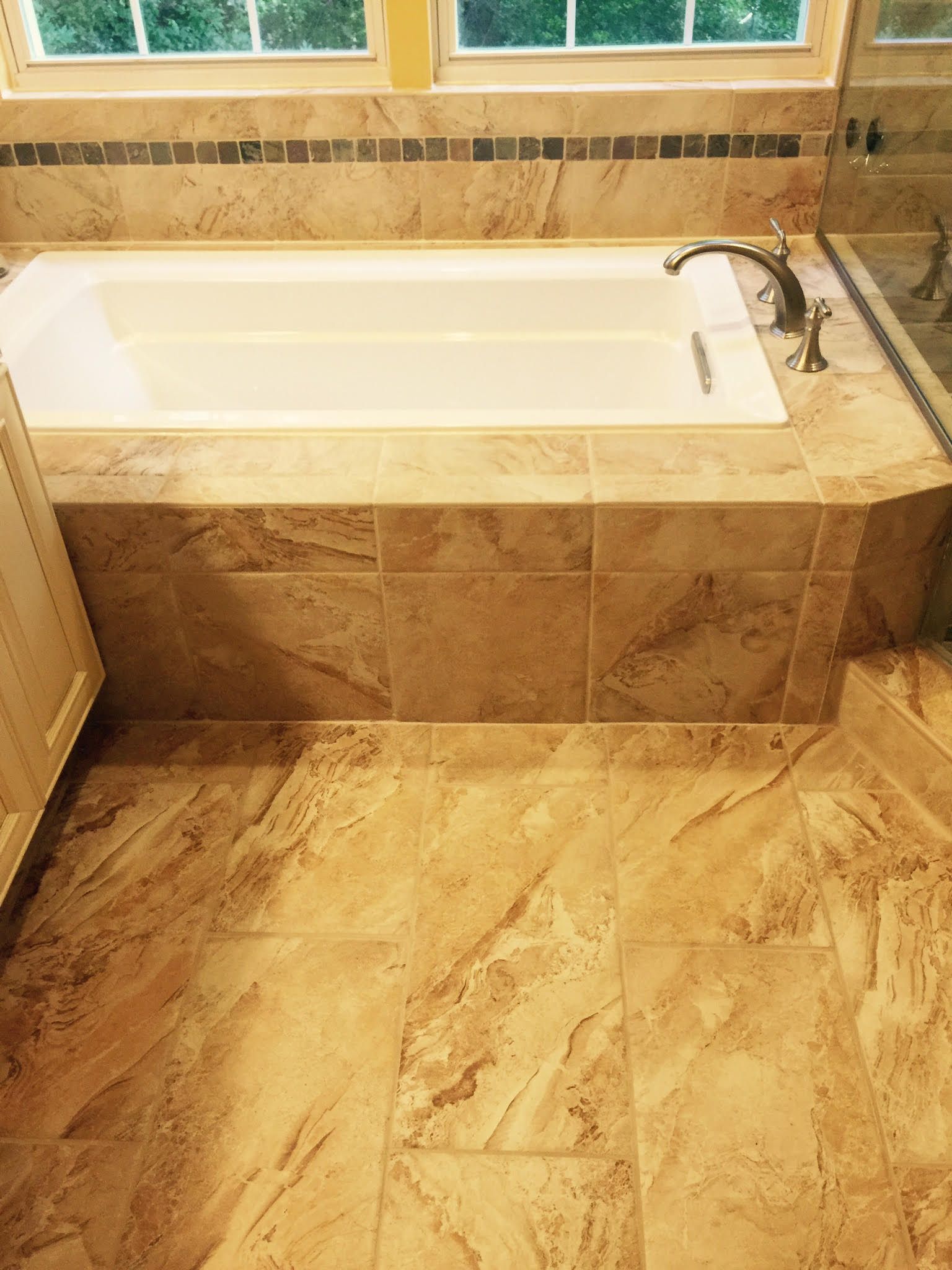 Bathroom with beige tile, a white bathtub, and a window.