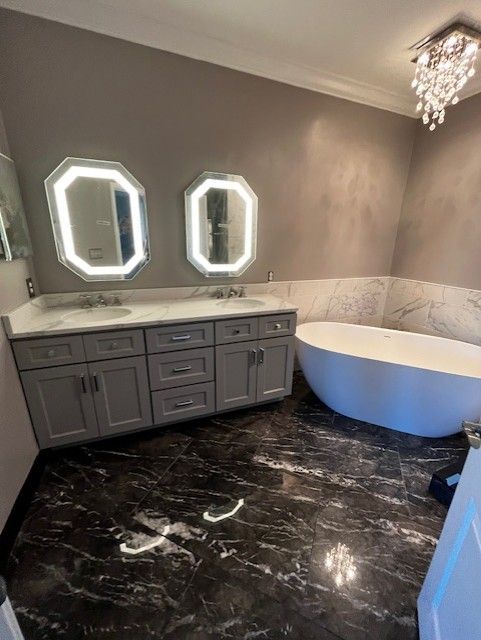 A luxurious bathroom with gray vanity, octagonal mirrors, soaking tub, and dark marble floor.