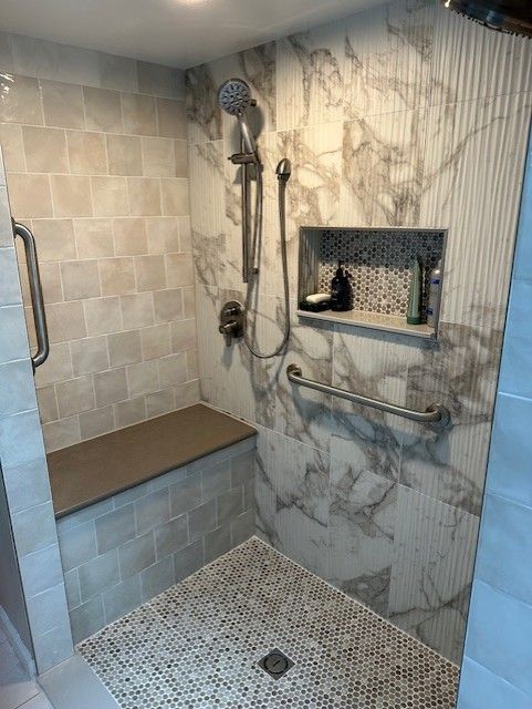 Shower with marble-look wall, pebbled floor, built-in seat, and grab bars for accessibility.