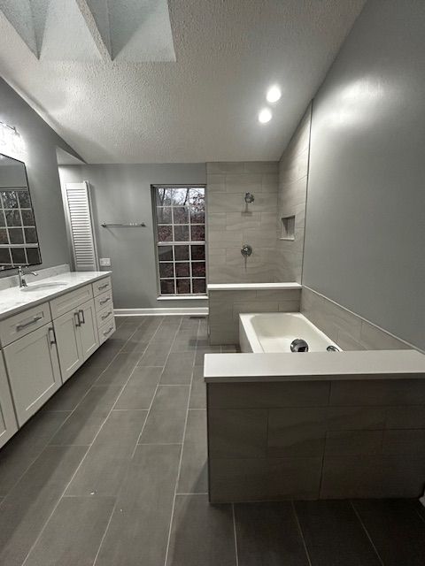 Gray and white bathroom with large vanity, soaking tub, and tiled shower.