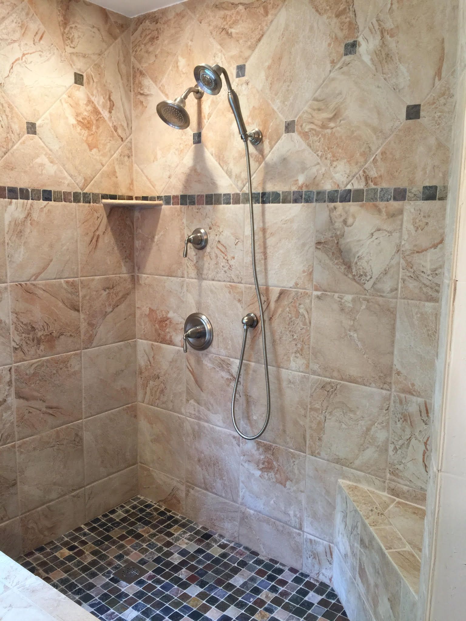 Shower with beige and brown patterned tiles, hand shower, and mosaic floor.