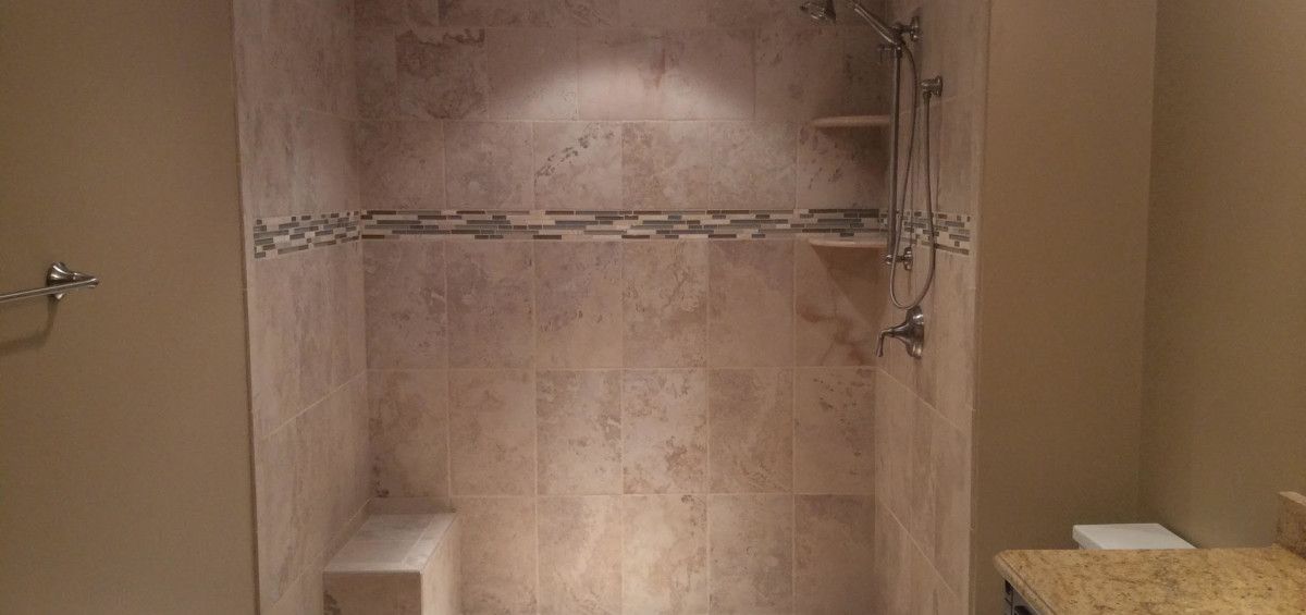 Tiled shower with a bench, shelf, and showerhead in a bathroom.