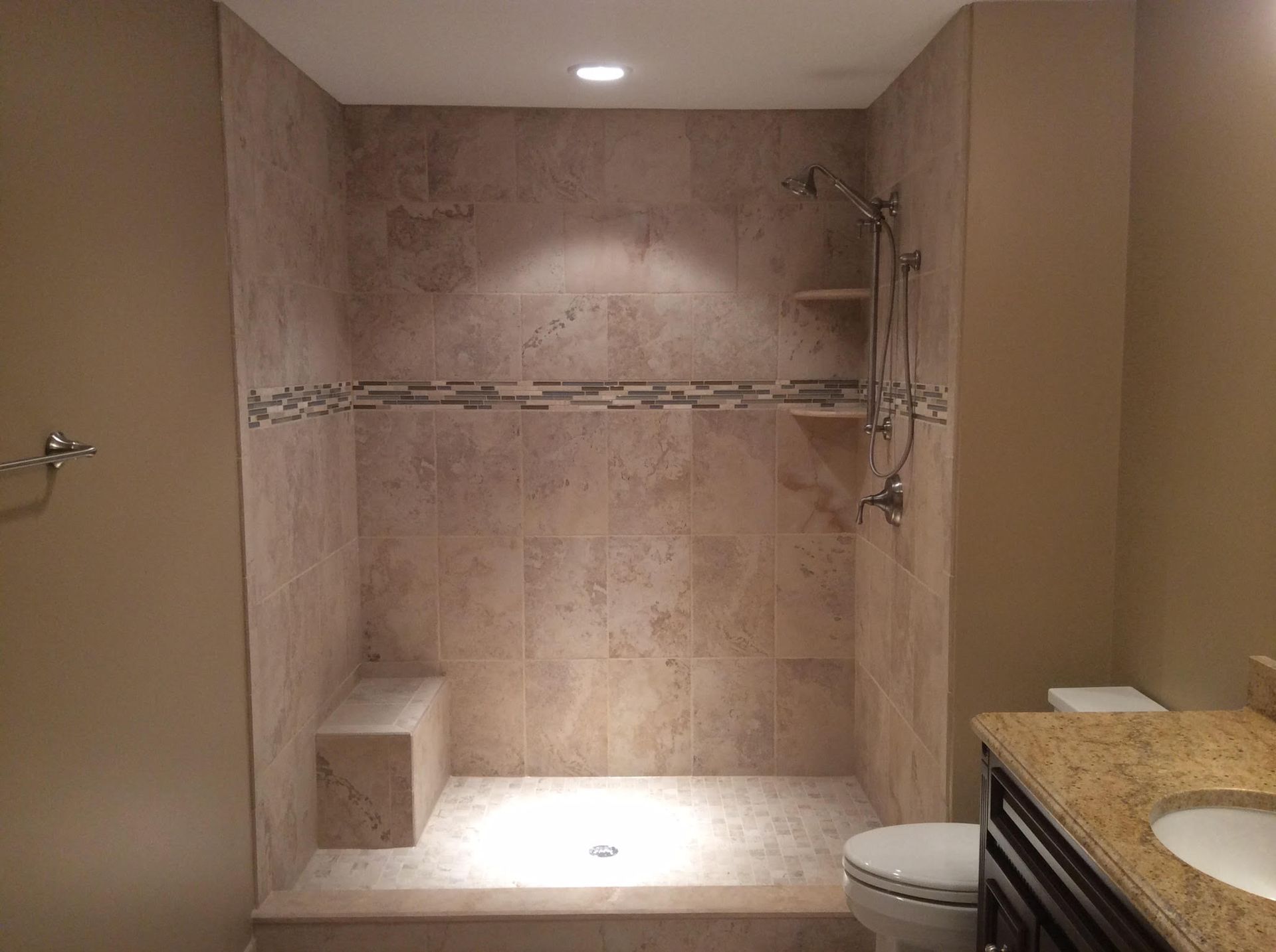 A beige tiled walk-in shower with a built-in seat and shelf, set in a bathroom with tan walls.