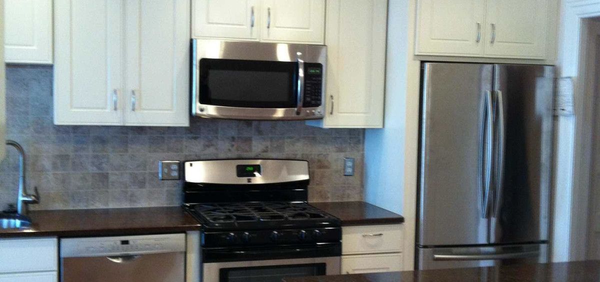 A kitchen with white cabinets, stainless steel appliances, dark countertops and tile backsplash.