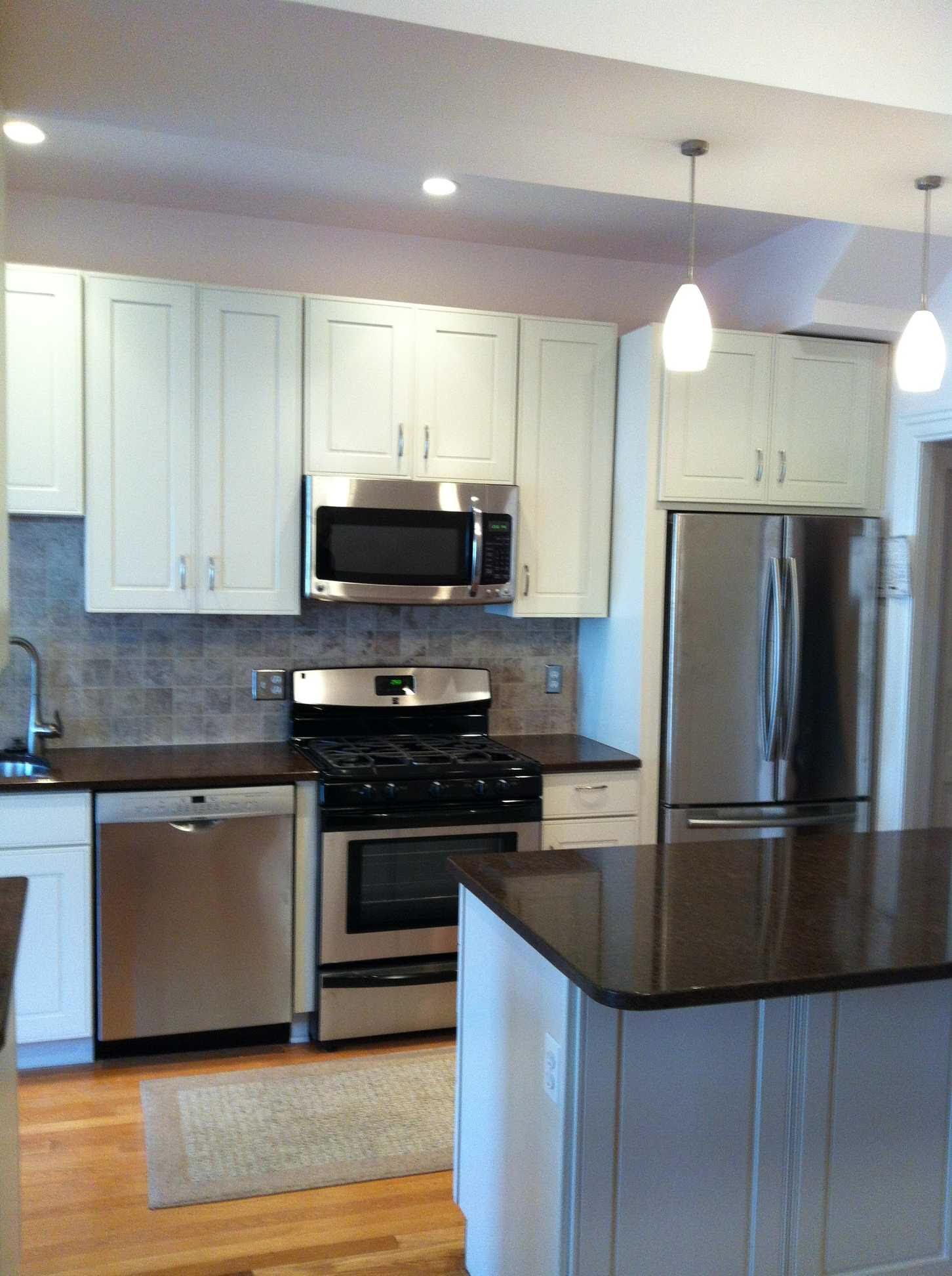 Modern kitchen with stainless steel appliances, white cabinets, and a dark countertop island.