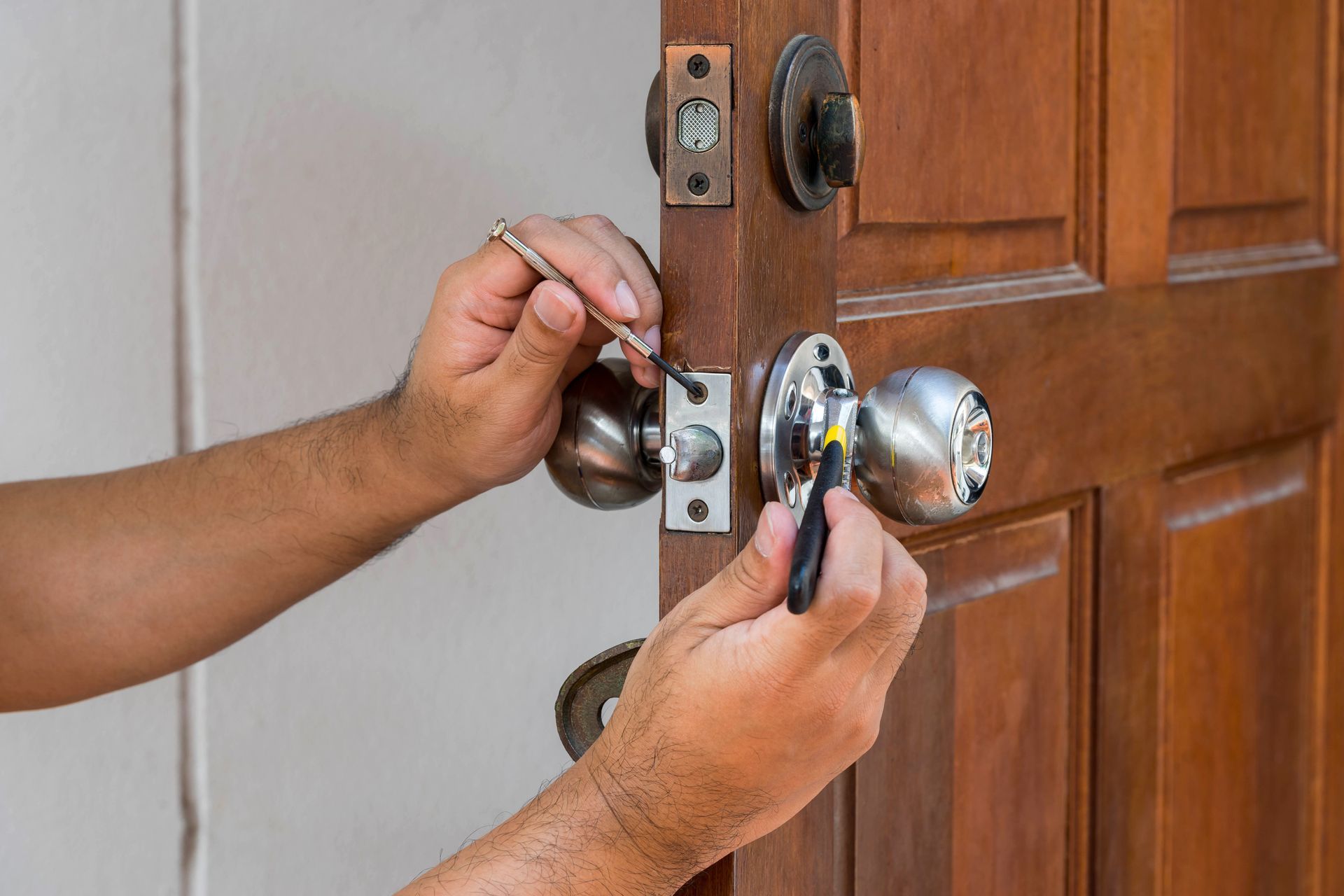 A man is fixing a door knob with a screwdriver.