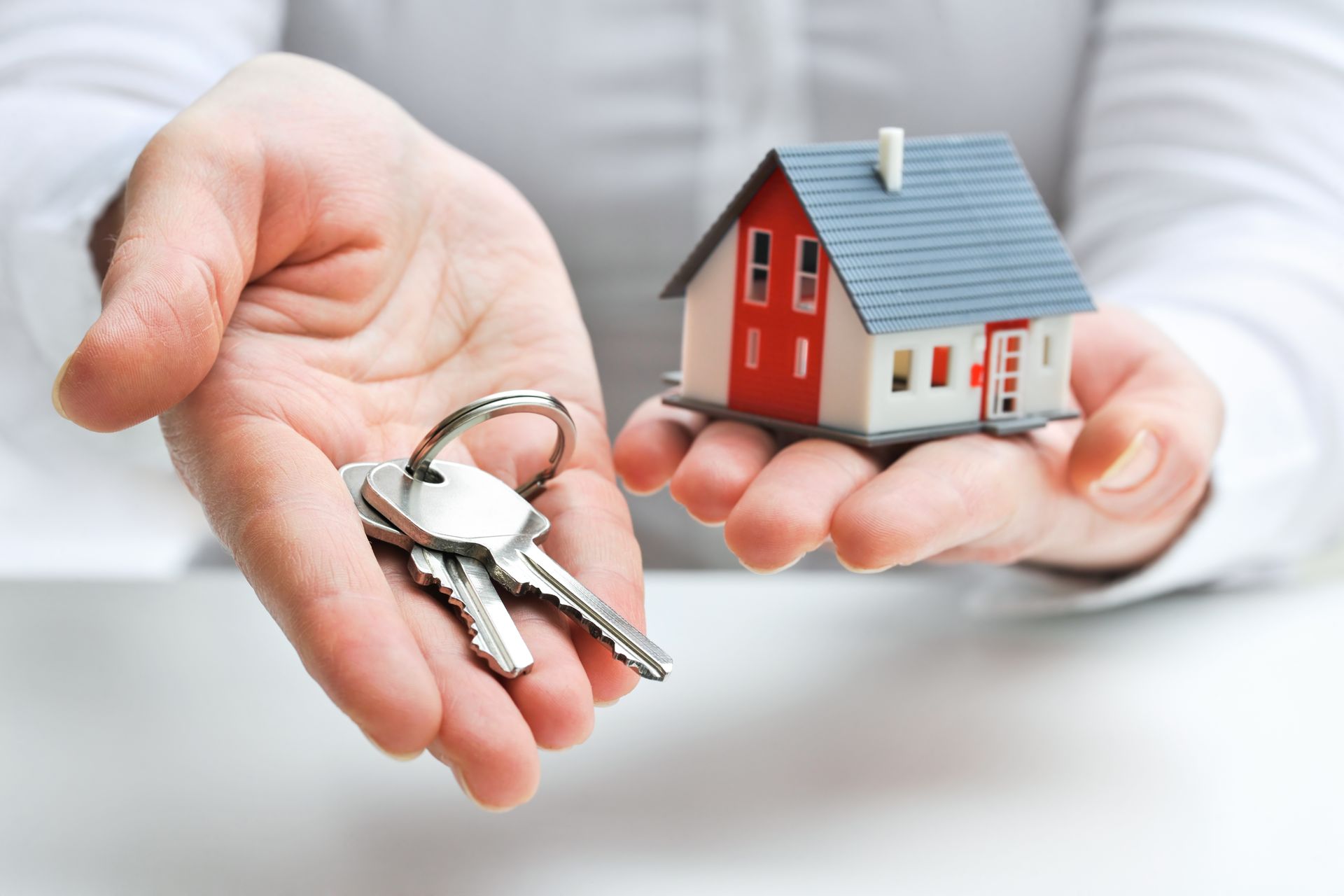 A person is holding a model house and keys in their hands.