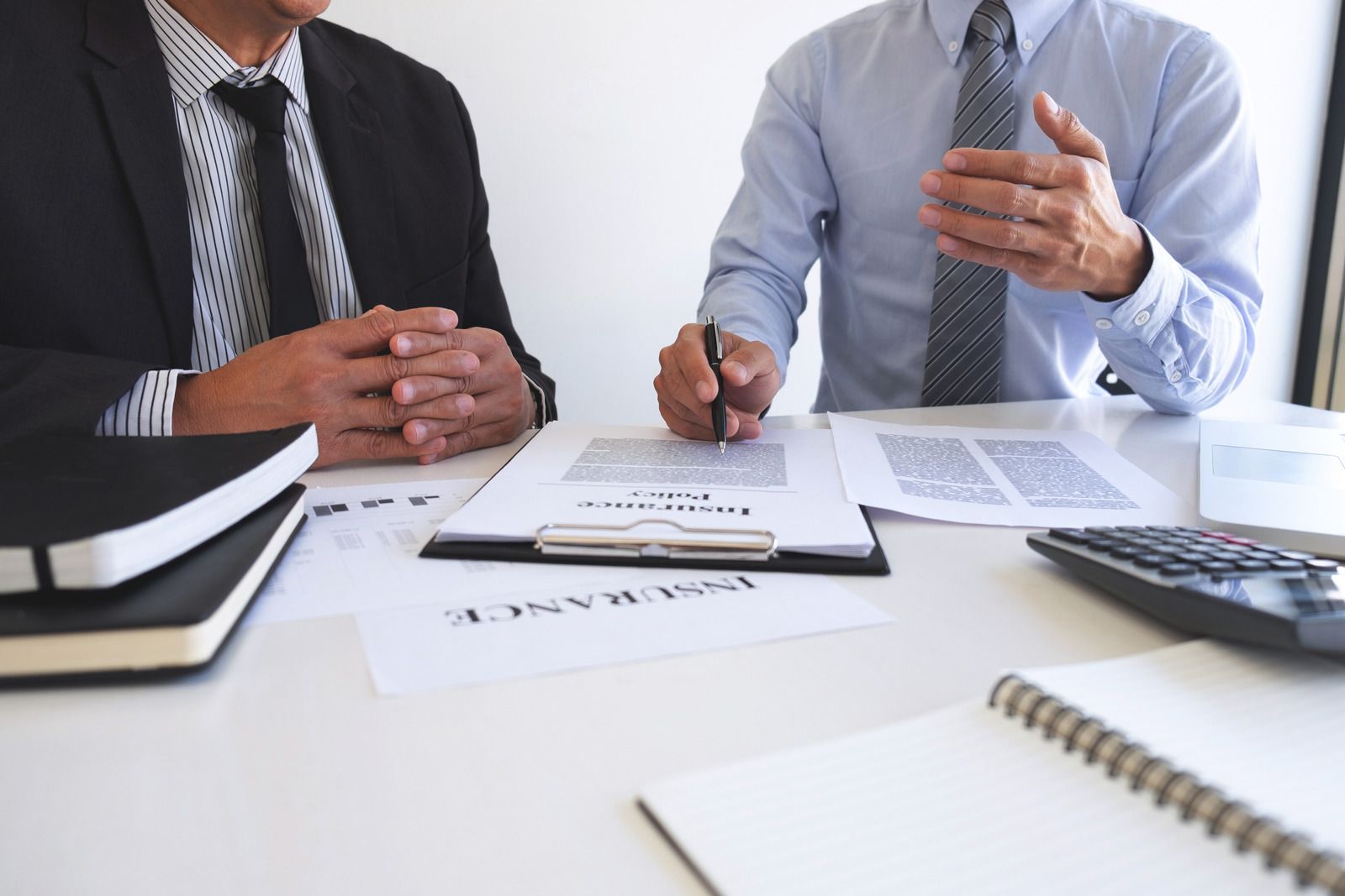 Two men are sitting at a table with papers and a calculator.