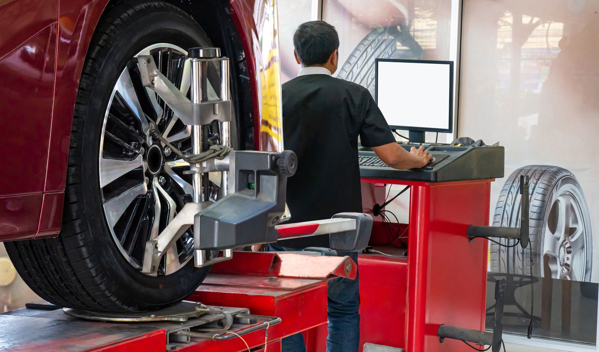 Car on red lift undergoing wheel alignment in an auto shop, technician at a computer console