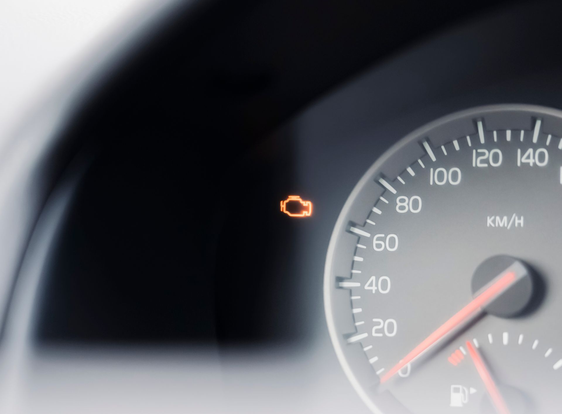 Car dashboard with orange check engine light on near the speedometer.