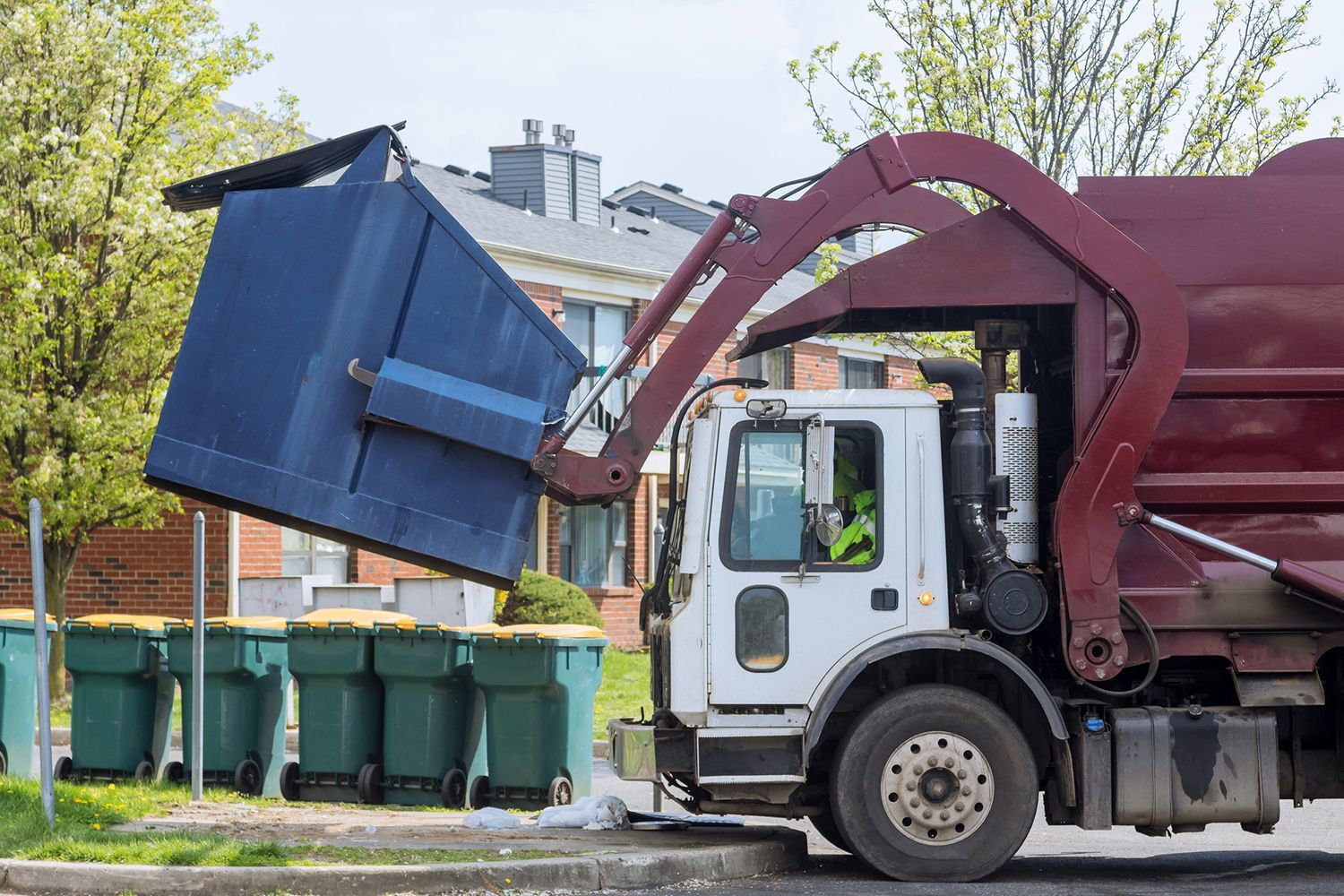 A red truck removes a skip bin from a residential street.
