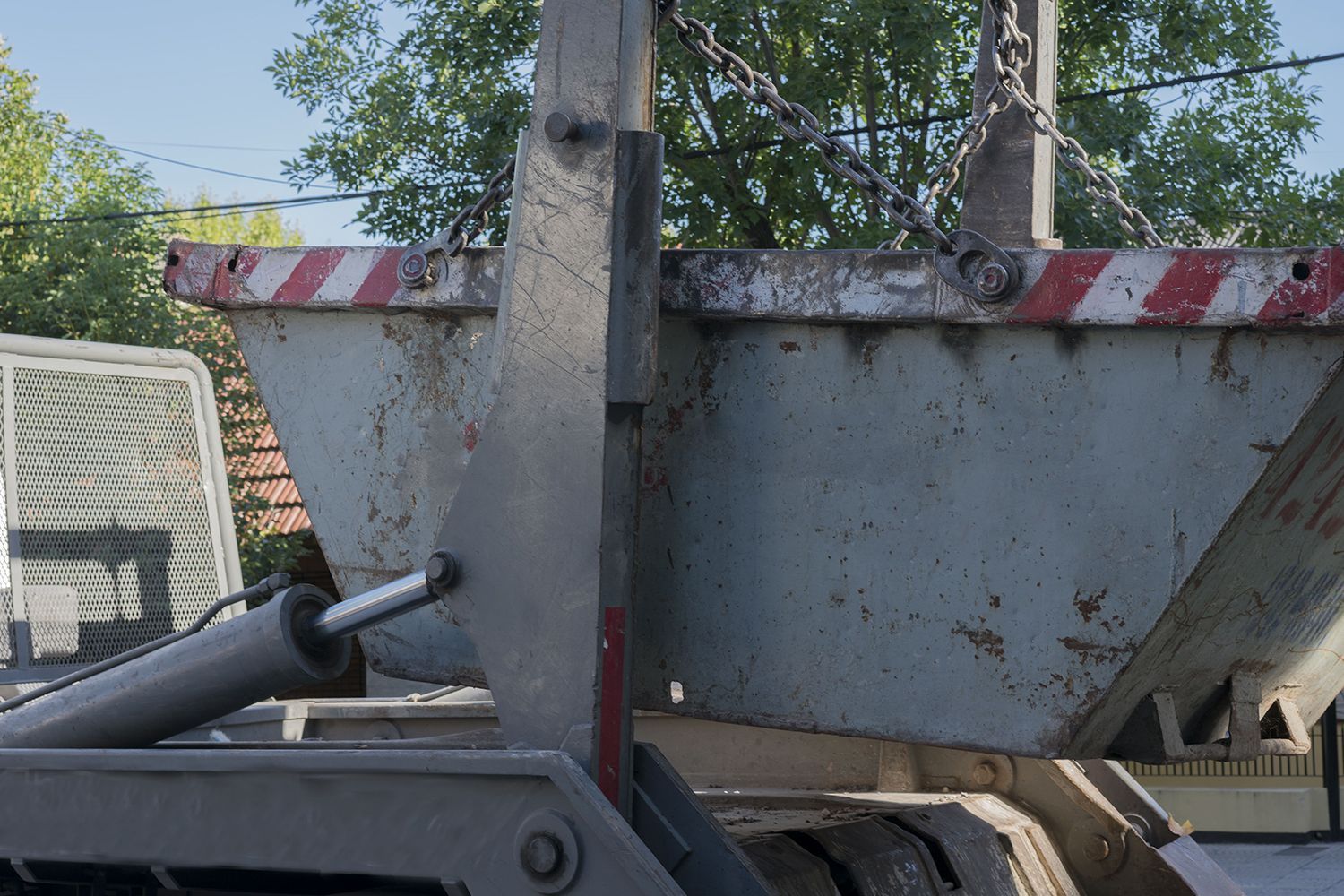 Detail of a skip bin loaded with debris being picked up by a truck on the street.