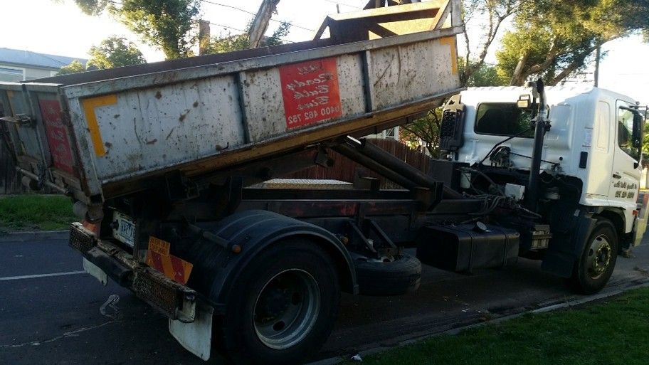 White truck with raised dumpster, parked on a street.