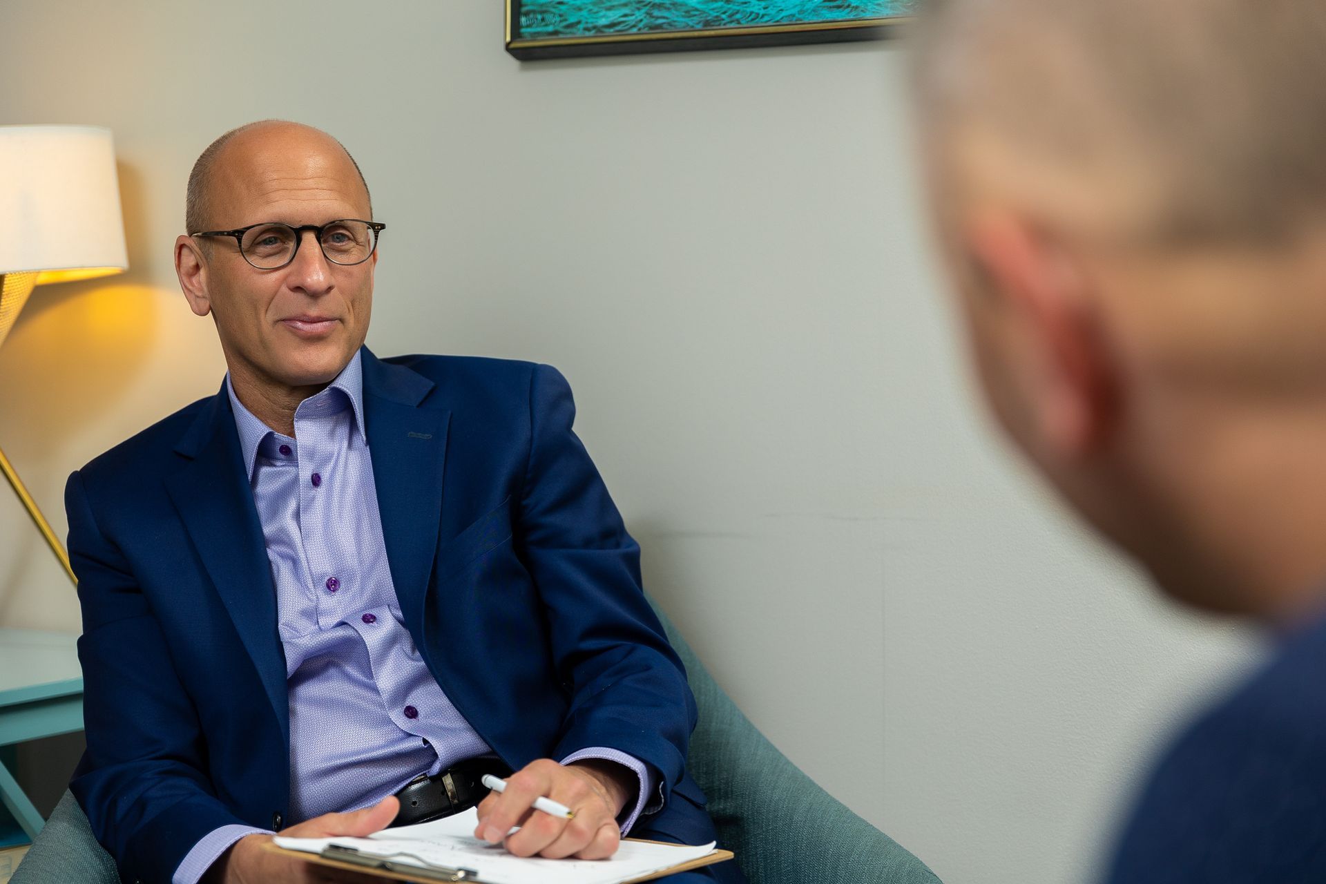 Man in a blue blazer speaking in an office, holding papers during a consultation