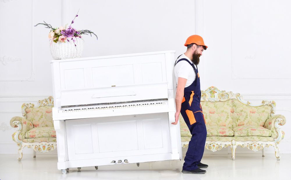 A Man is Carrying a White Piano in a Living Room — Davis Removals & Storage in Sydney, NSW