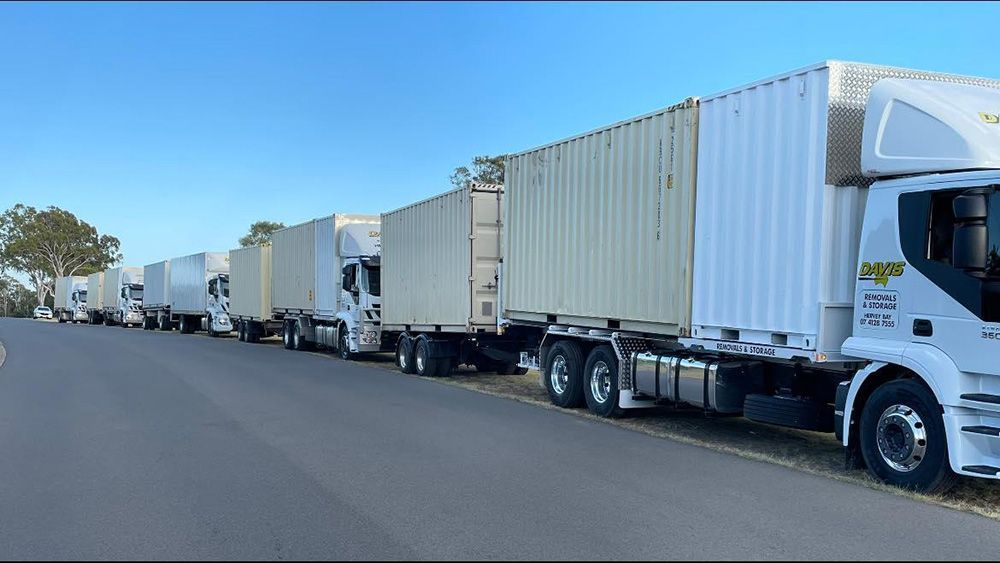 A Row of White Semi Trucks Are Parked on the Side of the Road — Davis Removals & Storage in Dundowran, QLD
