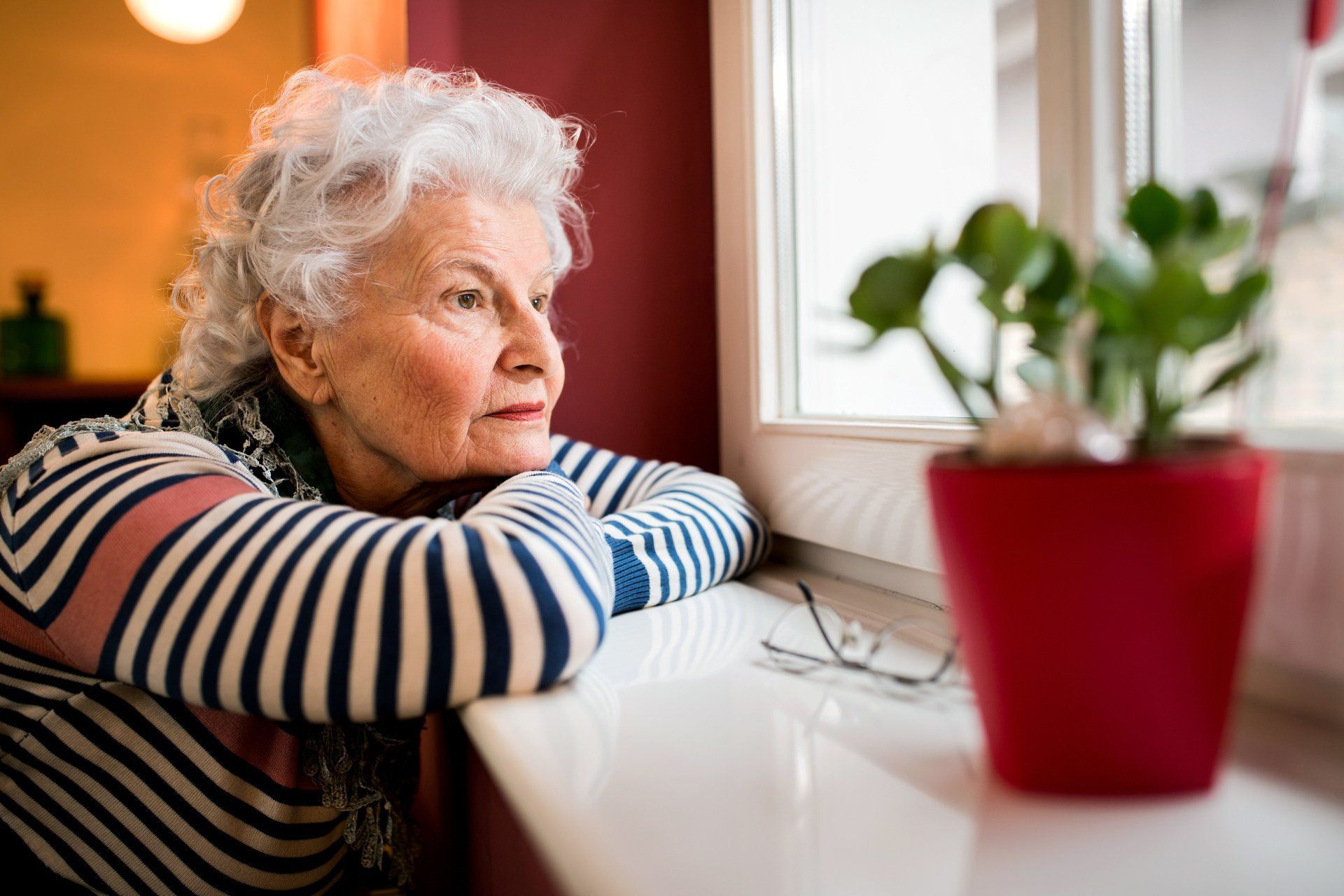 an elderly woman is leaning on a window sill looking out the window .