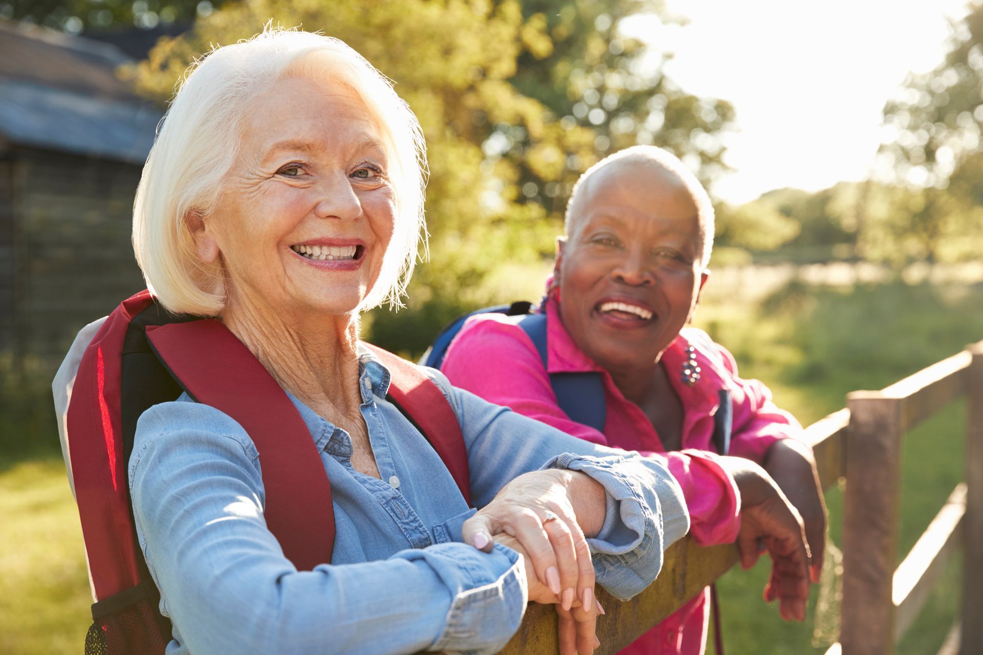 two elderly women with backpacks are standing next to each other and smiling .