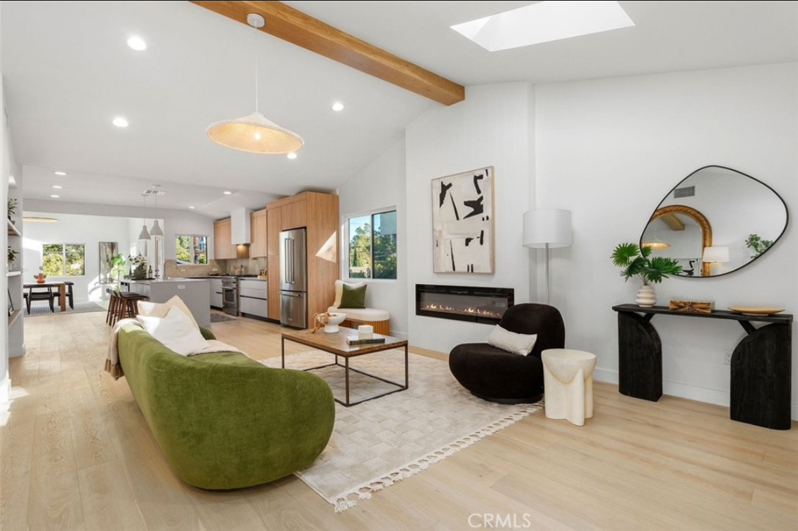 A modern open-plan living room with a green sofa, a dark accent chair, a fireplace, and light wood flooring.