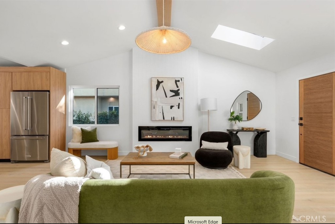 Modern living room with light wood floors, a green sofa, a fireplace, a large pendant light, and an entryway.