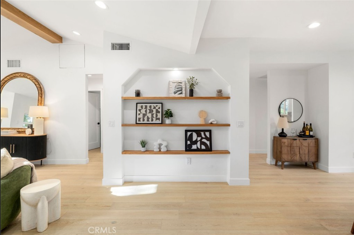 A bright, modern interior featuring white walls, light wood flooring, and built-in wooden shelves centered on a wall.