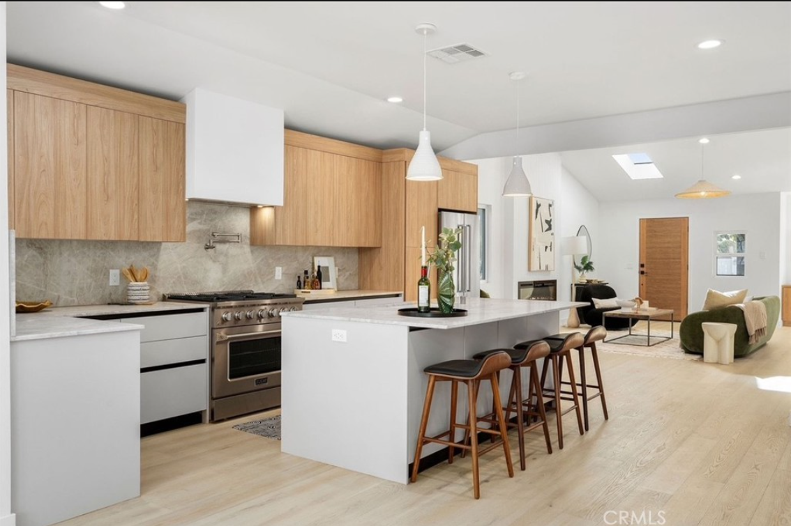 Modern open-concept kitchen with light wood cabinets, white island, bar stools, and a view into the living room.