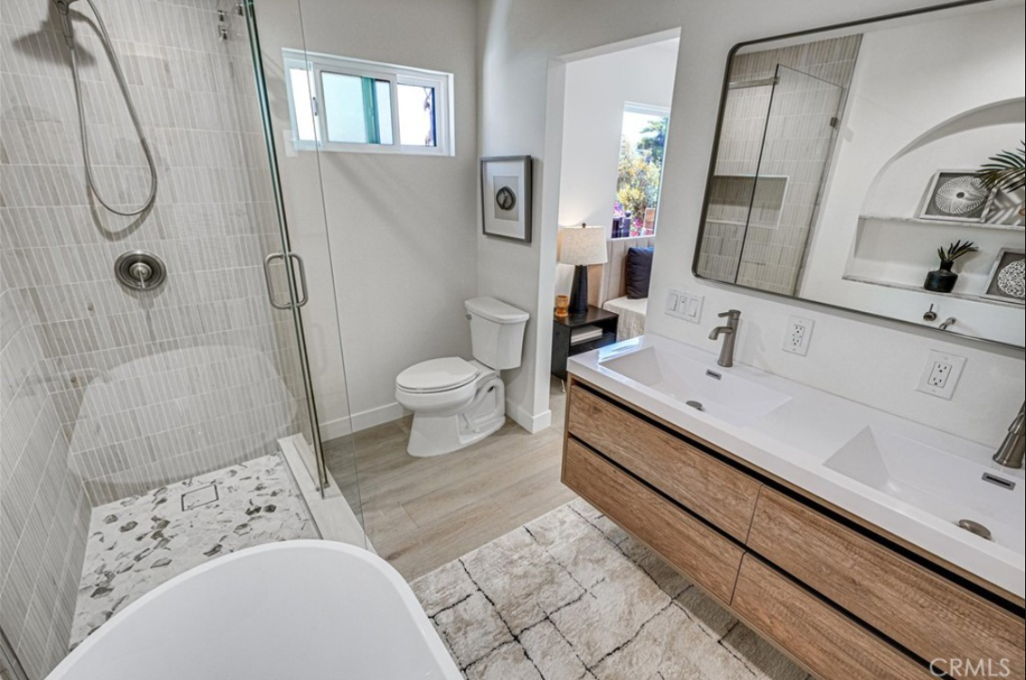 Modern bathroom with a glass-enclosed shower, a white soaking tub, a dual-sink wood vanity, and a toilet.