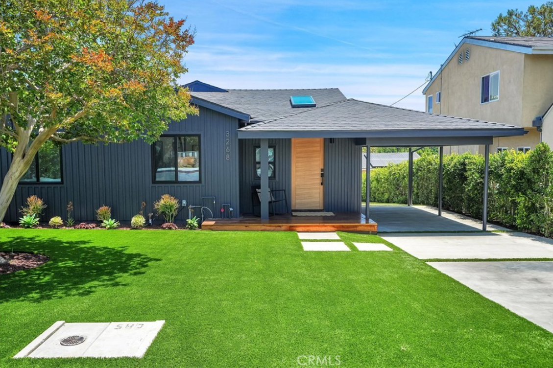 A modern one-story home with dark gray vertical siding, a natural wood door, and an attached carport over a driveway.