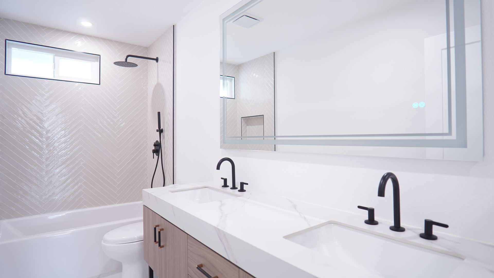 Modern bathroom with white countertops, double sinks, matte black faucets, and a herringbone-tiled bathtub enclosure.
