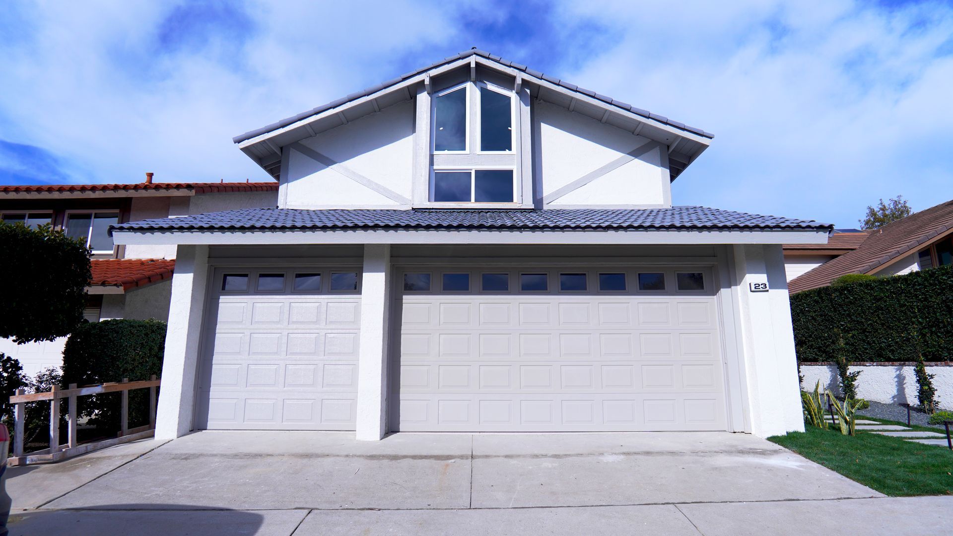 A two-story house with a three-car garage and light-colored siding under a blue sky with some clouds.