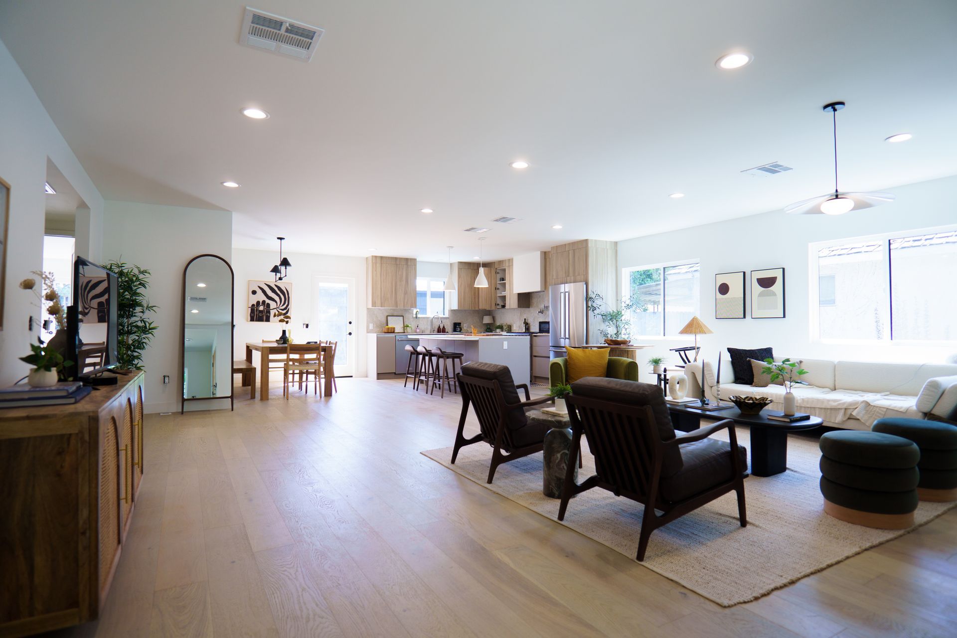 An open-concept living and kitchen space with light wood flooring, neutral furniture, and a dining area in the background.