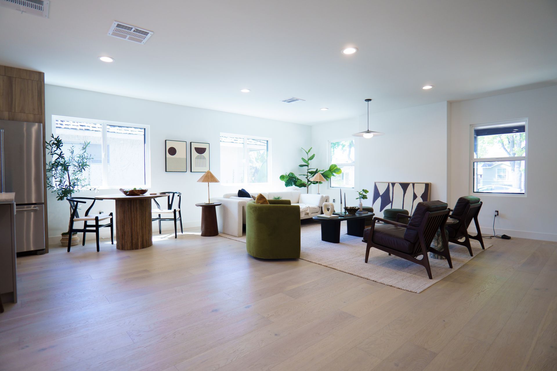 A modern, open-concept living and dining area with light wood floors, neutral furniture, and a green velvet armchair.