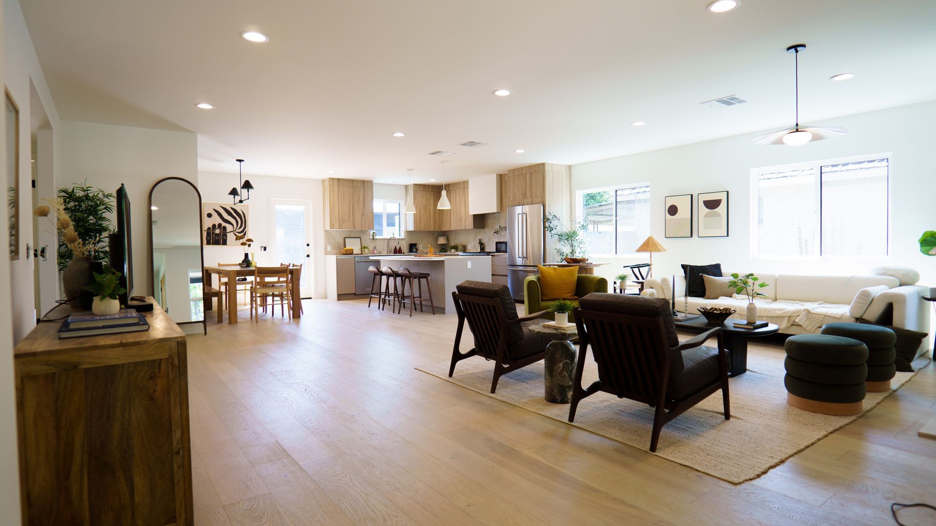 A bright, open-plan home featuring a modern kitchen, dining area, and living room with dark seating and hardwood floors.