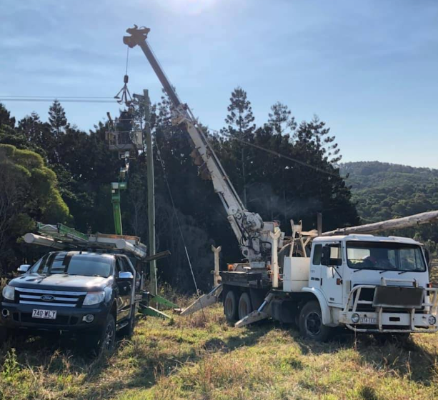 Truck with crane replacing power pole in wooded area; a car is parked nearby— Gold City Solar & Electrical in Long Flat, QLD