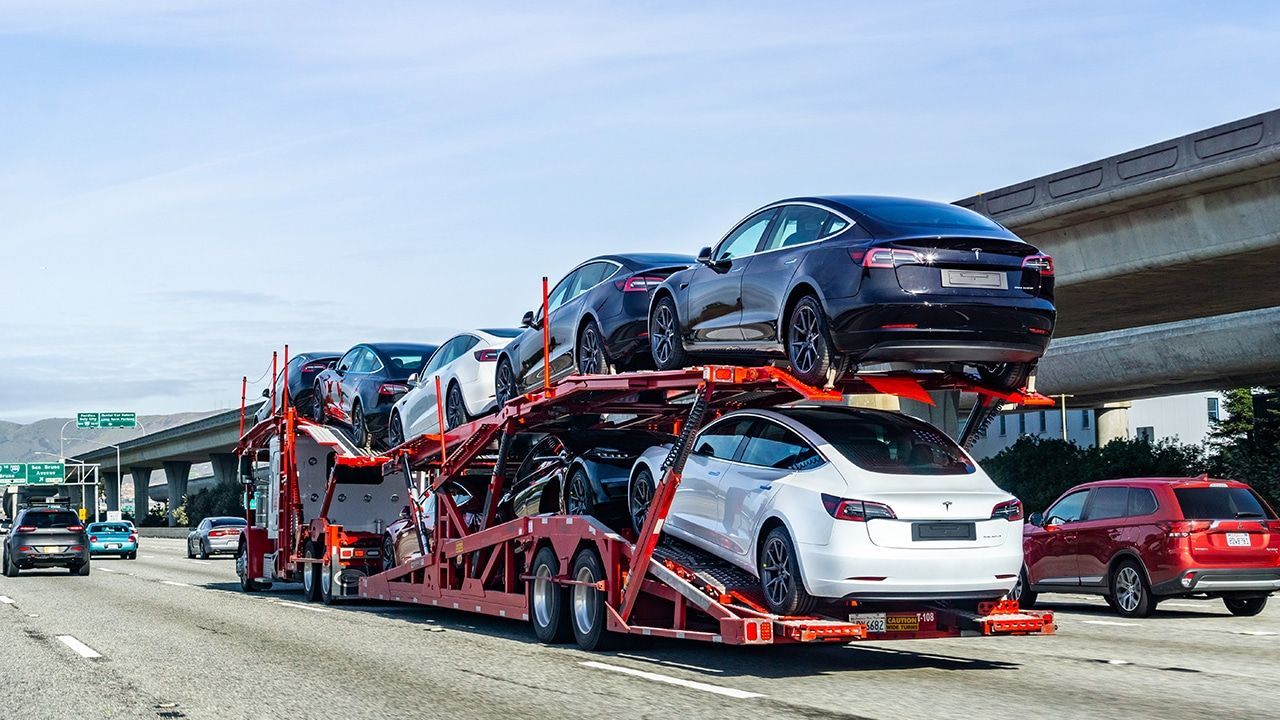 A truck is carrying two cars on top of each other on a highway.