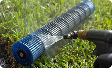 A cylindrical air handler fan being washed with a hose on green grass.