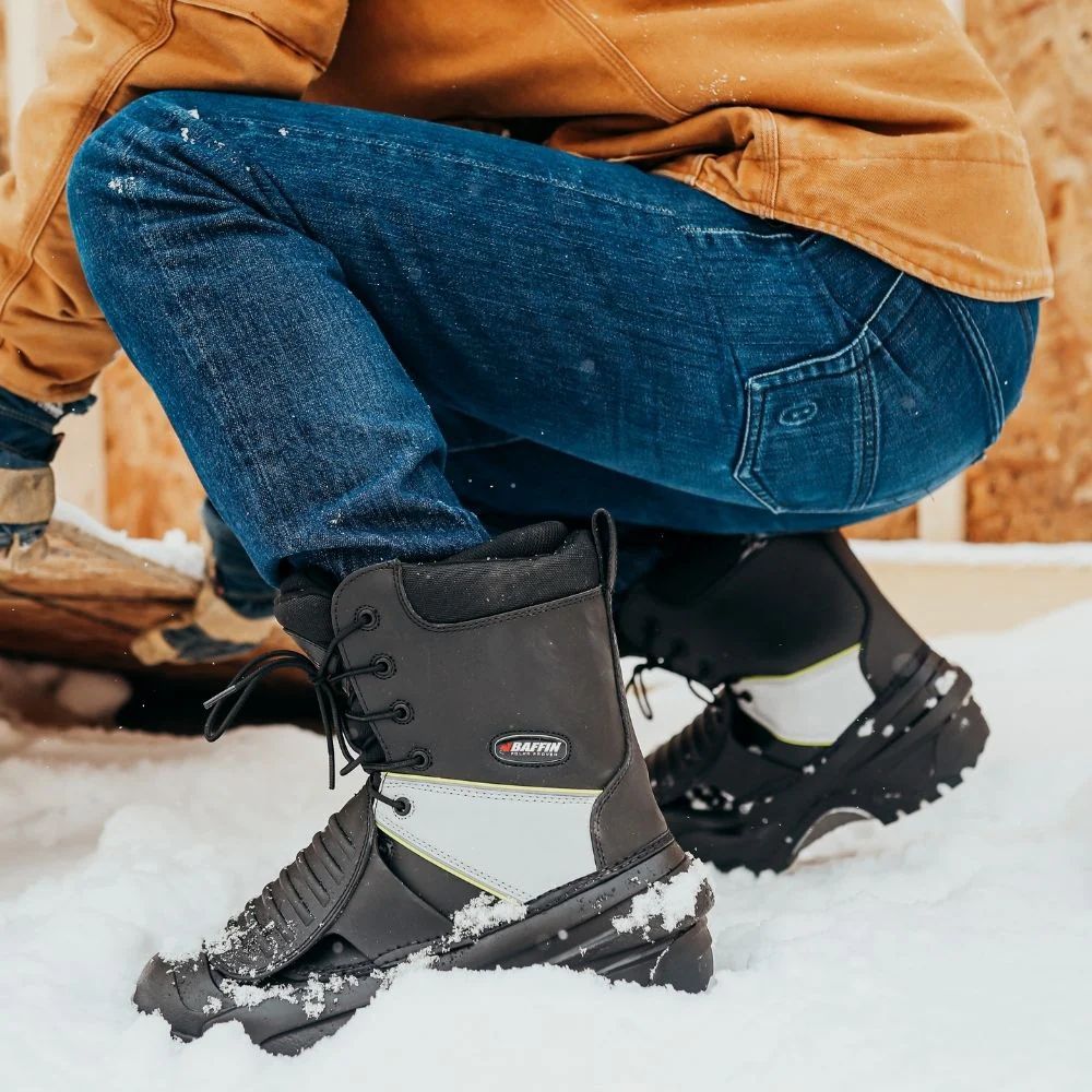 Worker in blue coveralls and hard hat tending to a chemical container near red pipes.
