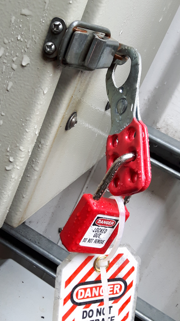 A red lock with a danger tag is attached to a metal latch on a beige panel.