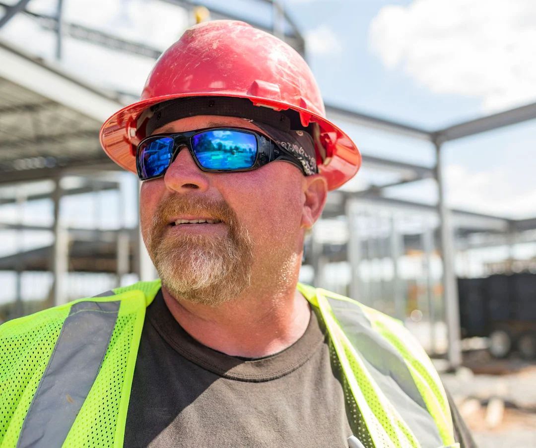 Safety equipment, including hard hats, respirators, safety glasses, gloves, and ear protection, arranged on wood.