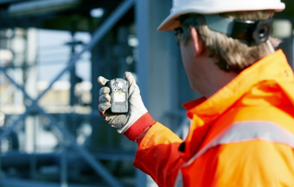 Person in safety gear inspecting equipment with a handheld device at a construction site.