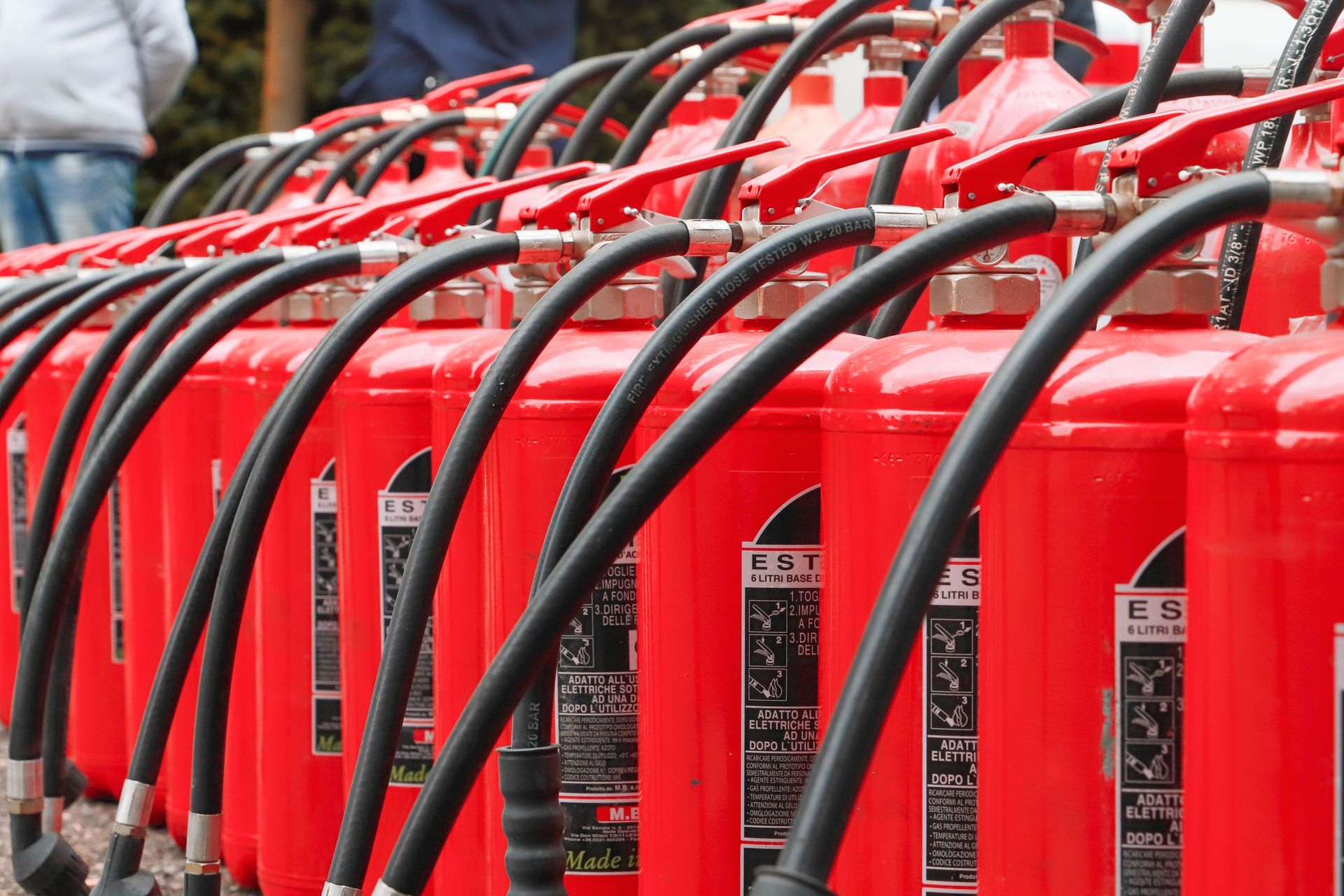 Row of red fire extinguishers with black hoses and handles.