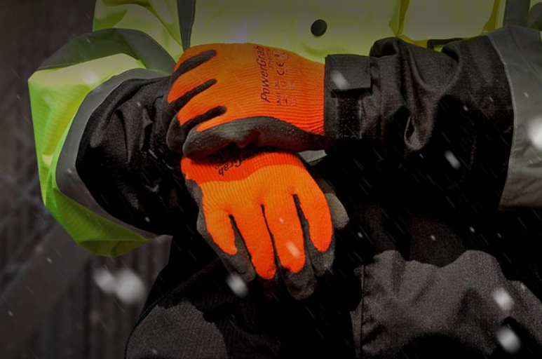 Person wearing orange and black work gloves, snow falling.