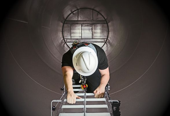 Person in a hard hat climbing a ladder inside a large, cylindrical structure.