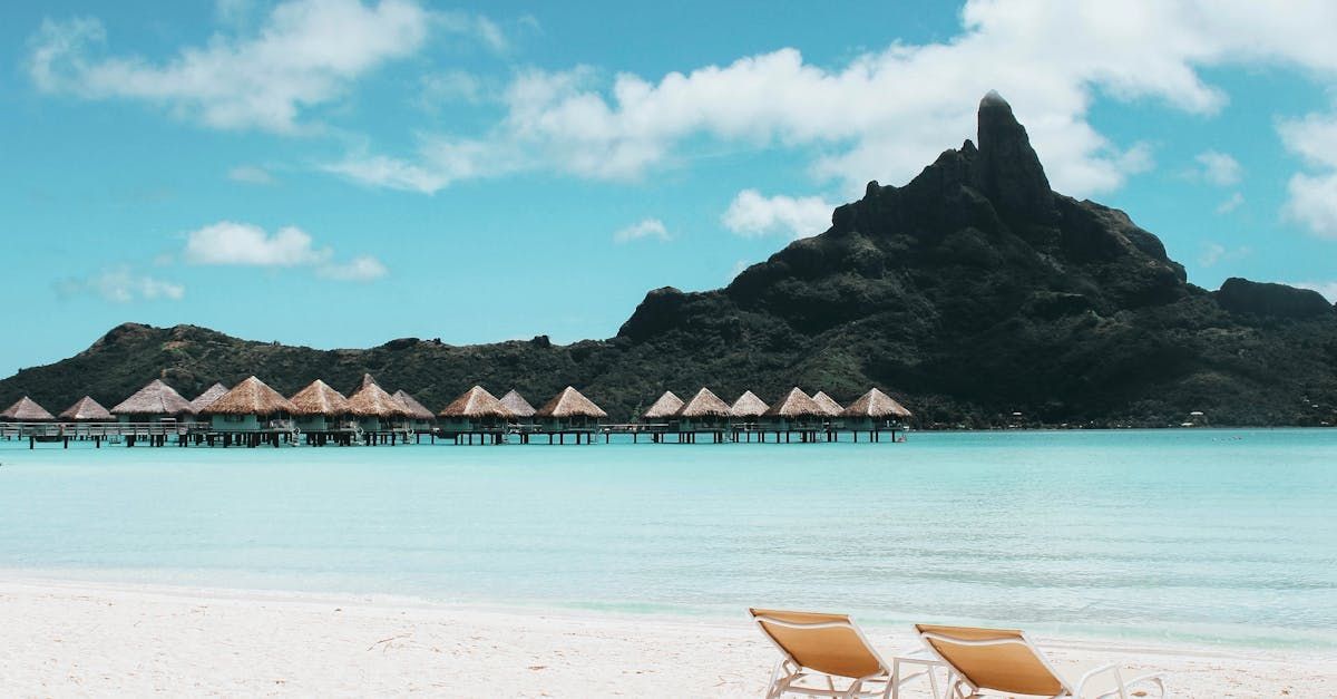 There are two chairs on the beach with a mountain in the background.