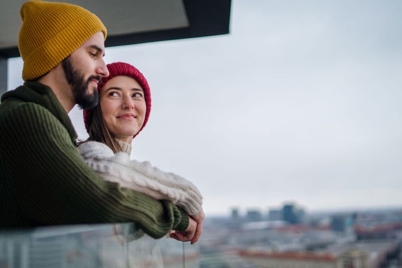 A man and a woman are standing on a balcony looking out over a city.