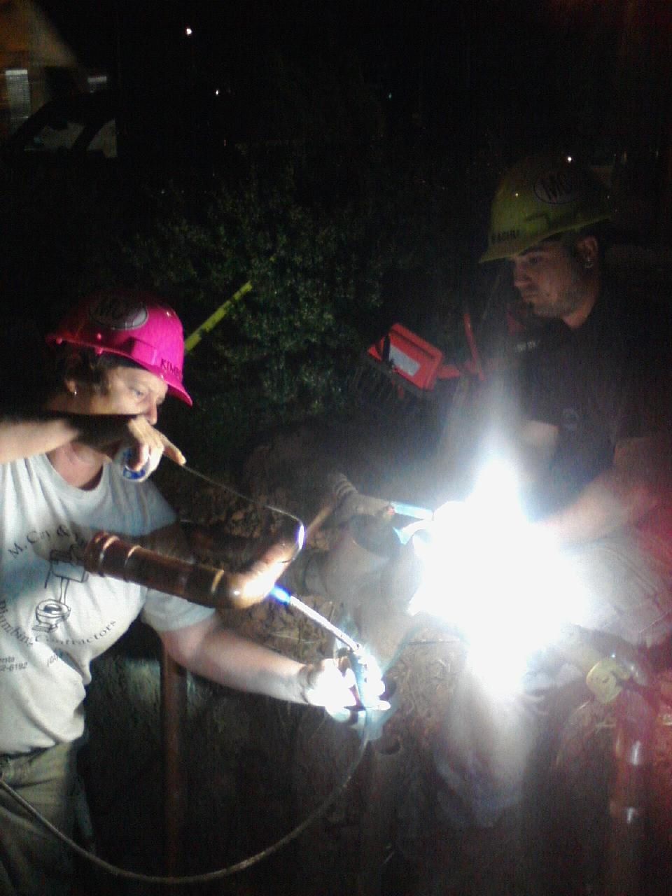 A man wearing a pink hat is welding in the dark.