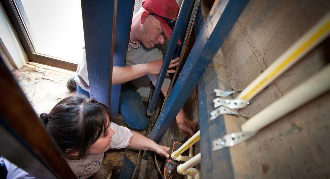 A man and a woman are working on a pipe in a room.